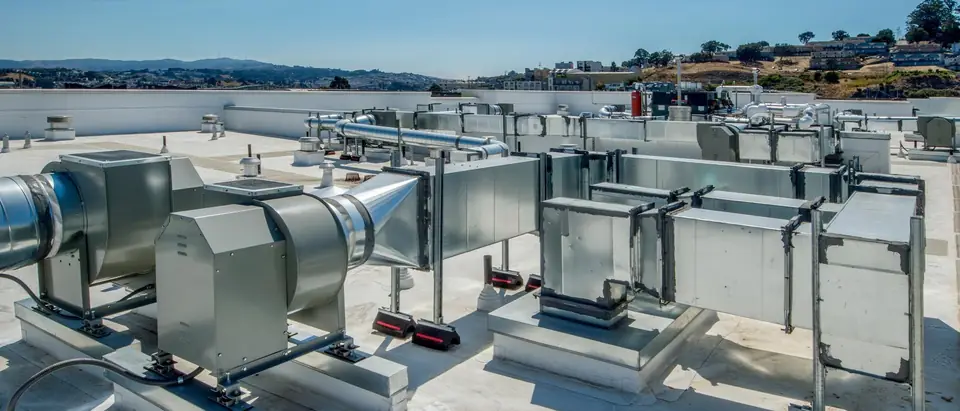 White membrane flat roof with metal ductwork and exhaust fans, dry hills and blue sky beyond