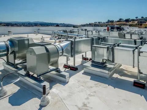 White membrane flat roof with metal ductwork and exhaust fans, dry hills and blue sky beyond