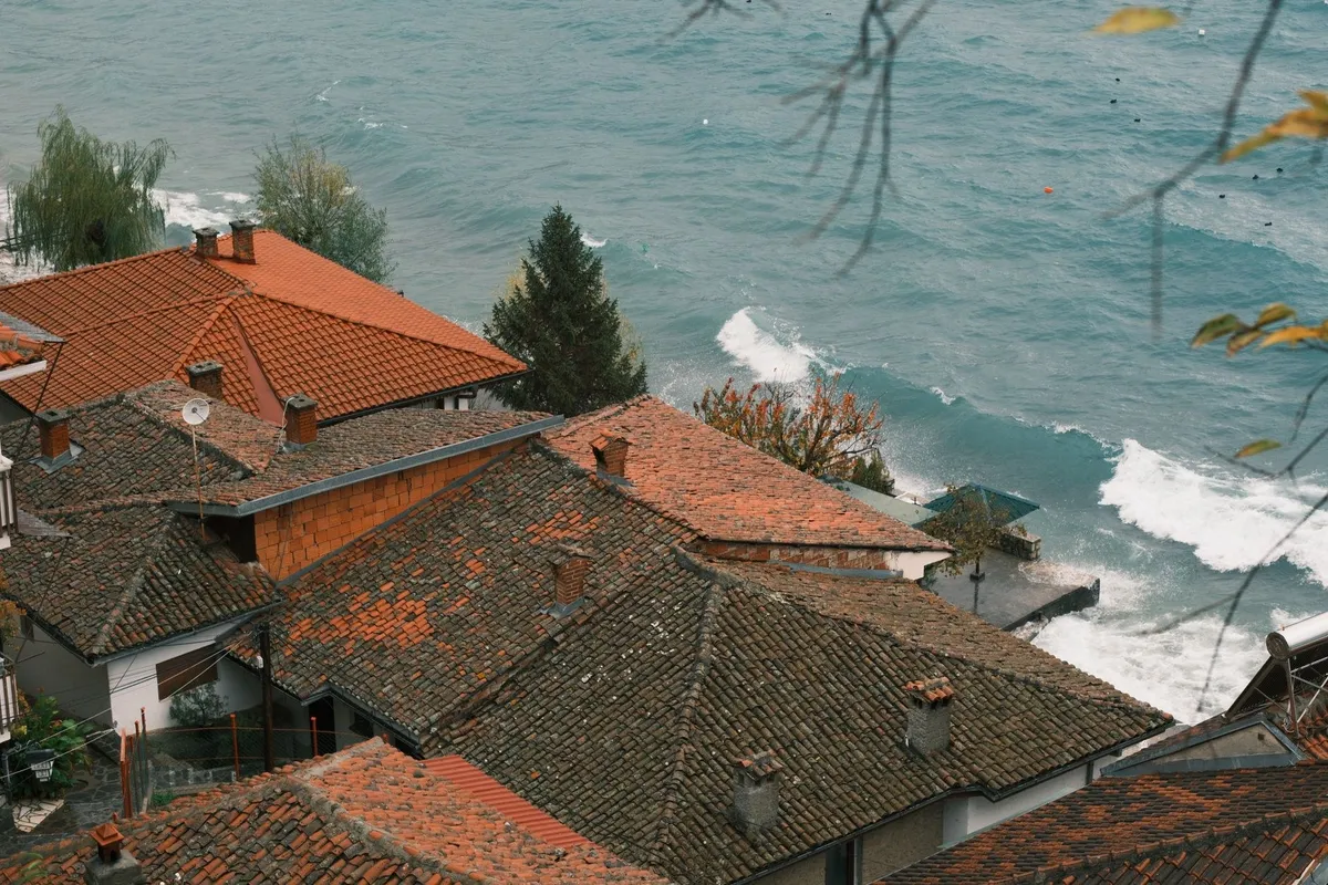 Aerial view of rustic village rooftops next to a calm ocean, reflecting the charm of coastal living.